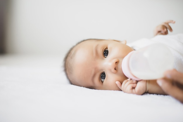Adorabile piccolo neonato asiatico che dorme e beve latte su un comodo letto al mattino