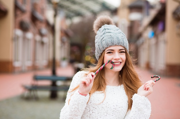 Adorabile ragazza bionda che si diverte con un bastoncino di zucchero natalizio per strada