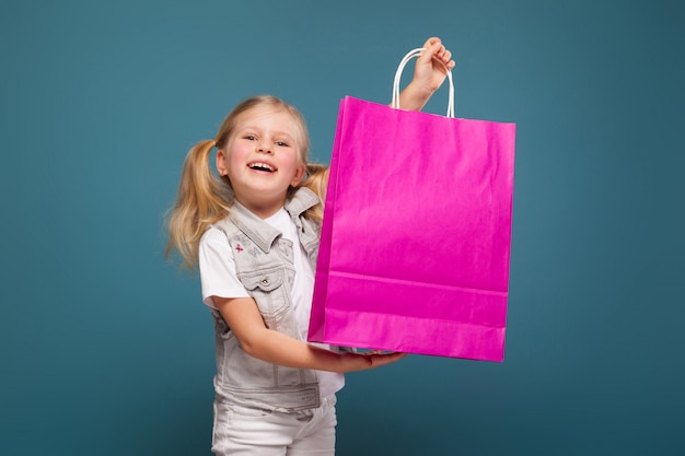 Adorabile ragazza carina in camicia bianca, giacca bianca e pantaloni bianchi tenere sacchetto di carta viola