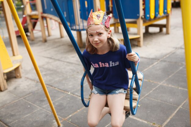 Adorabile ragazza che si diverte sull'oscillazione del parco giochi nel parco