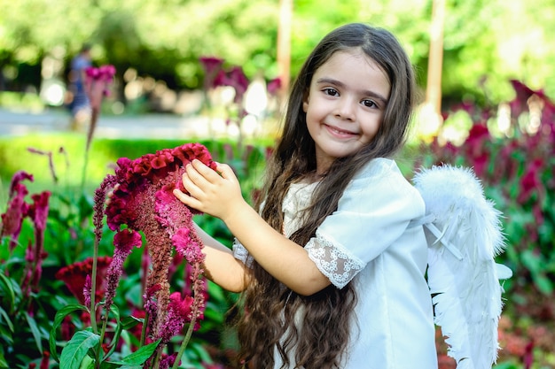 adorabile ragazza che tocca il fiore di amaranto in giardino con colori vivaci dopo il rituale del battesimo