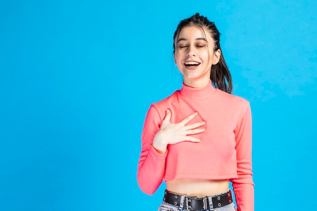 Adorabile ragazza chiude gli occhi e si mette la mano sul petto su sfondo blu Foto di alta qualità