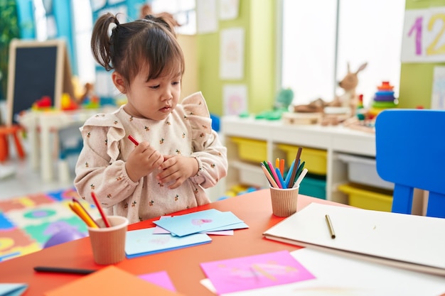 Adorabile ragazza cinese studente in età prescolare disegno su carta in piedi all'asilo