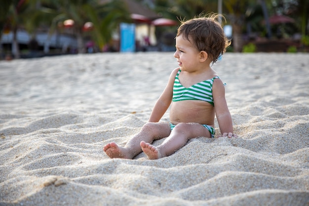 adorabile ragazza in costume da bagno si siede su una spiaggia di sabbia sotto il sole.