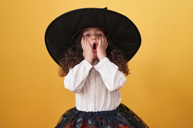 Adorabile ragazza ispanica che indossa il costume di halloween in piedi con espressione sorpresa su sfondo giallo isolato