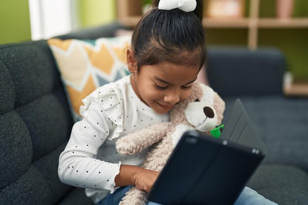 Adorabile ragazza ispanica che utilizza il touchpad seduto sul divano di casa