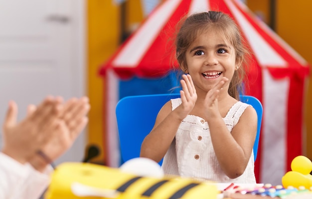 Adorabile ragazza ispanica seduta sul tavolo che applaude all'asilo