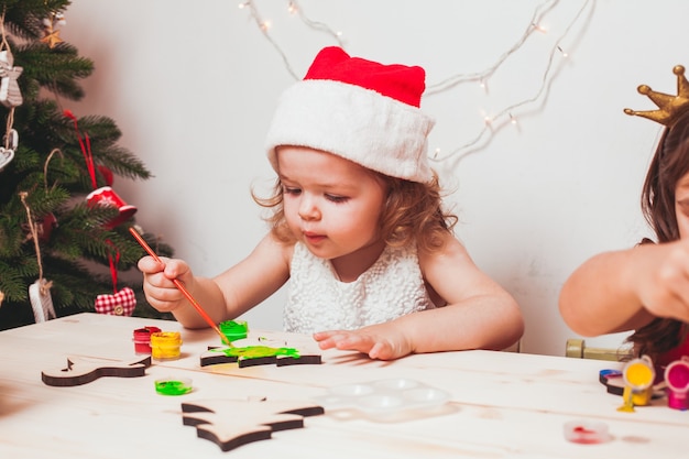 Adorabile ragazza sta dipingendo figurine di Natale in legno