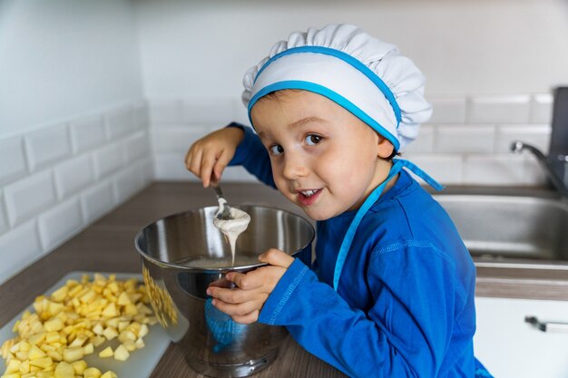 Adorabile ragazzino aiutando e cuocendo la torta di mele nella cucina di casa, al coperto