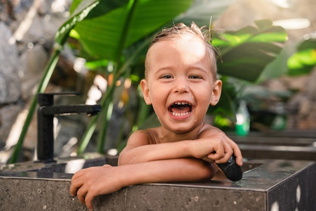 Adorabile ragazzino che gioca e fa il bagno in un lavandino di pietra all'aperto