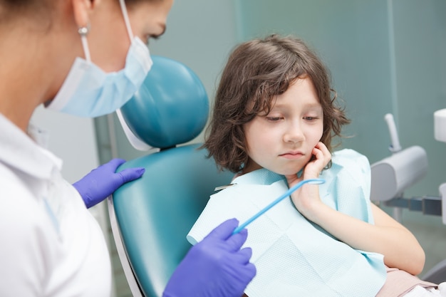 Adorabile ragazzino che ha mal di denti, seduto sulla poltrona del dentista in clinica