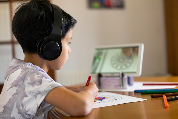 Adorabile ragazzo che dipinge un mandala con i suoi pennarelli colorati guardando un tutorial sul suo tablet