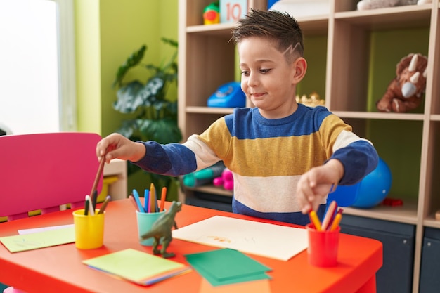 Adorabile ragazzo ispanico studente in età prescolare seduto sul tavolo disegno su carta all'asilo