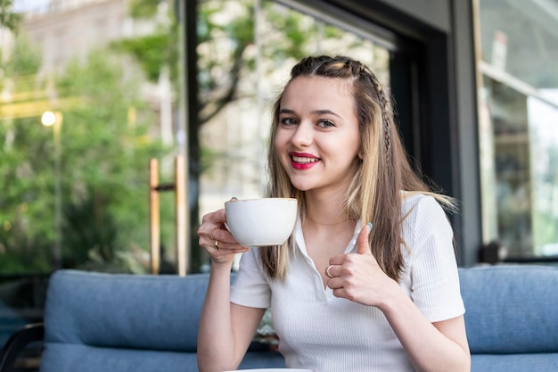 Adorabile signora che tiene tazza di caffè e gesto pollice in su