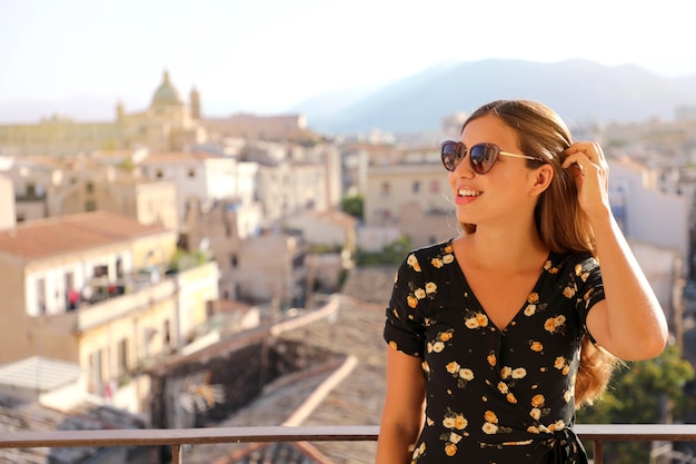 adorabile signora con lunghi capelli castani in posa sulla terrazza su sfondo sfocato della città