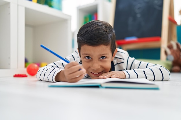 Adorabile studente ragazzo ispanico che scrive sul taccuino all'asilo