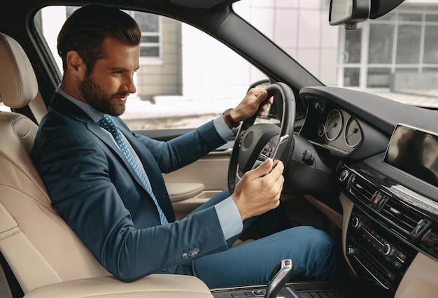 Adorabile uomo sicuro di sé in abbigliamento formale che legge un messaggio sul cellulare in auto