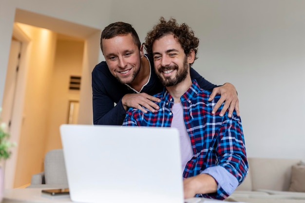 Adorabili coppie gay che ridono insieme mentre si siedono nel loro soggiorno a casa Due romantici giovani amanti maschi che si divertono a navigare in internet al chiuso Giovane coppia gay che vive insieme