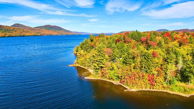 Aerea sul lago con foresta di alberi autunnali che copre la costa e acque blu