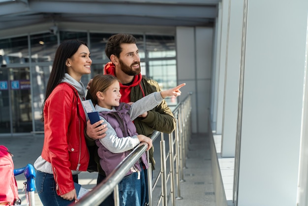 Aerei così grandi. Vita verticale della giovane famiglia con i bagagli in piedi vicino alla finestra in aeroporto prima dell'imbarco