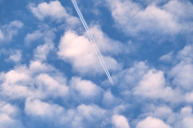 Aereo a reazione passeggeri distante che vola in alta quota attraverso nuvole bianche sul cielo blu lasciando dietro di sé una traccia di fumo bianco di scia. Concetto di trasporto aereo