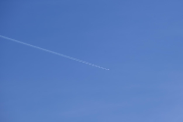 Aereo a reazione passeggeri distante che vola in alta quota su cielo blu chiaro lasciando traccia di fumo bianco di scia dietro Concetto di trasporto aereo