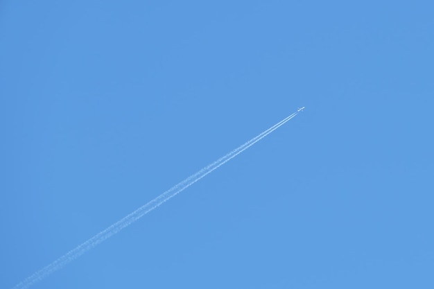 Aereo a reazione passeggeri distante che vola in alta quota su cielo blu chiaro lasciando traccia di fumo bianco di scia dietro Concetto di trasporto aereo