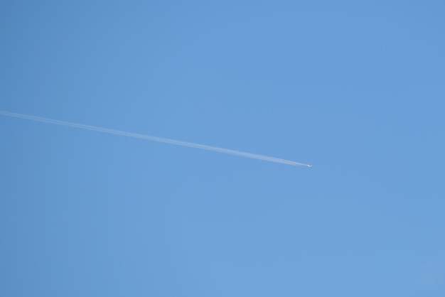 Aereo a reazione passeggeri distante che vola in alta quota su cielo blu chiaro lasciando traccia di fumo bianco di scia dietro Concetto di trasporto aereo