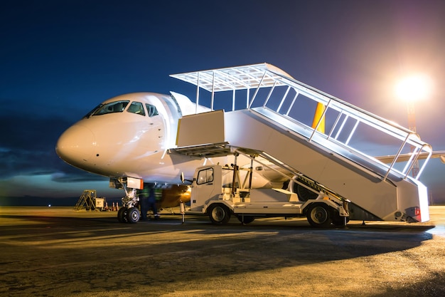 Aereo passeggeri bianco con scale di imbarco al piazzale dell'aeroporto notturno