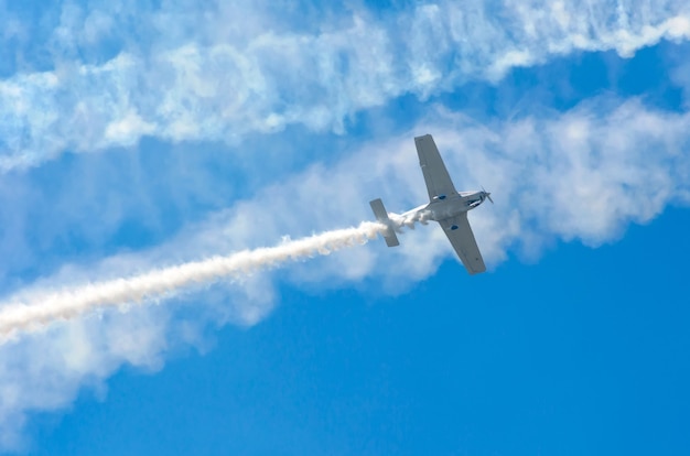 Aereo turboelica bianco con una traccia di fumo bianco contro un cielo blu.