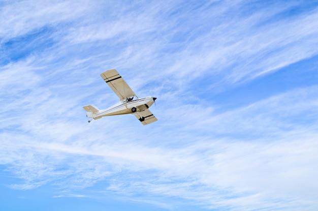 Aereo ultraleggero monomotore che vola nel cielo blu con nuvole bianche.