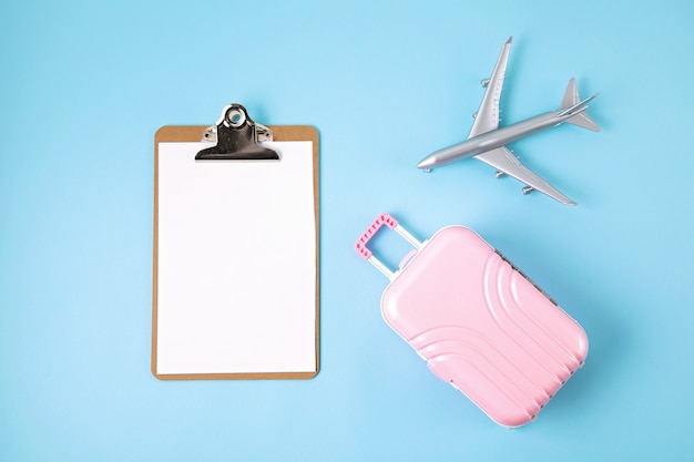 Aeroplano e valigia in miniatura sulla parete blu. Preparazione del viaggio, turismo, compagnie aeree, voli low cost, concetto di imballaggio bagagli. Vista dall'alto, piatto.