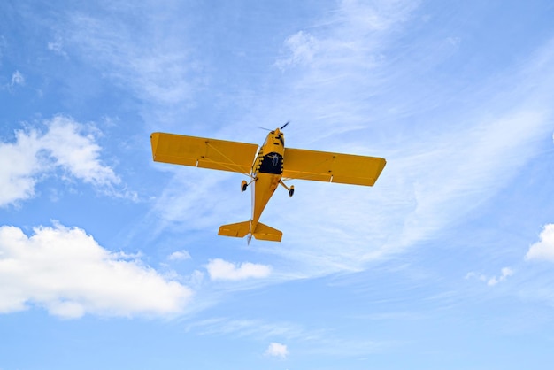 Aeroplano giallo monomotore ultraleggero che vola nel cielo blu con nuvole bianche