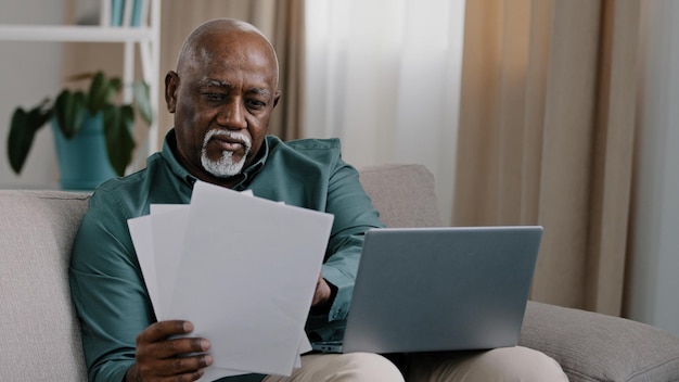 Affari afroamericano senior con documenti anziani uomo calvo imprenditore che scrive sul portatile