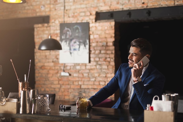 Affari allegri parlando al telefono, seduti al bancone del bar, bevendo whisky e avendo una conversazione piacevole e di successo, copia spazio