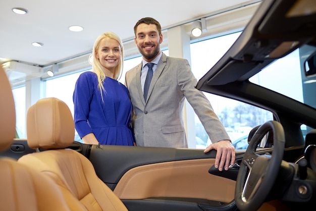 affari automobilistici, vendita di automobili, consumismo e concetto di persone - coppia felice che acquista auto in auto show o salone