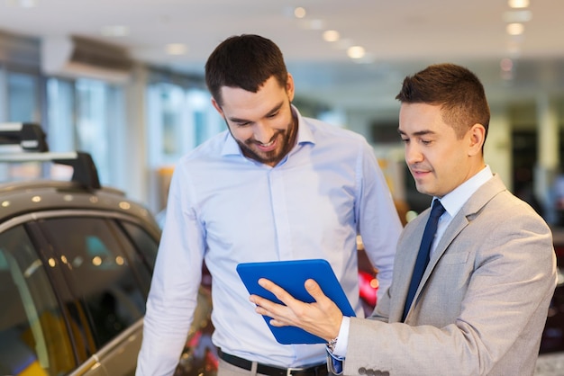 affari automobilistici, vendita di automobili, tecnologia e concetto di persone - uomo felice e rivenditore di auto con computer tablet pc in auto show o salone