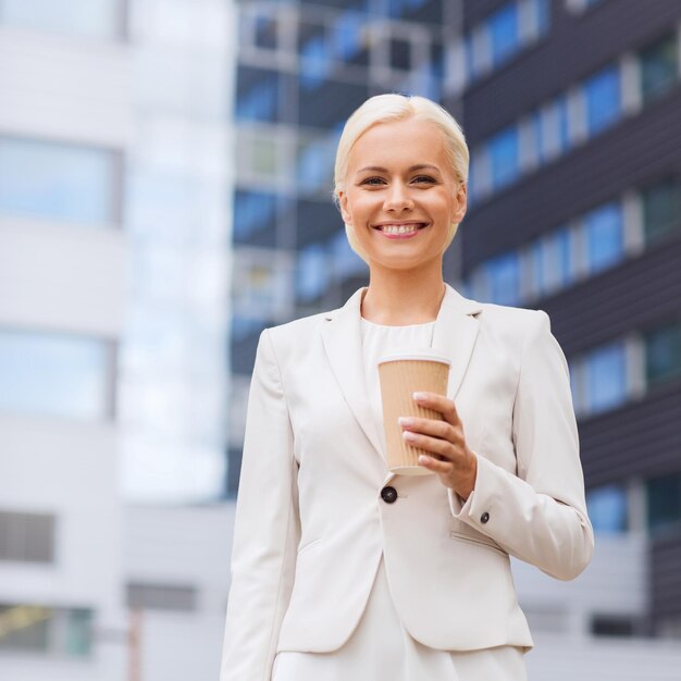 affari, bevande calde e persone e concetto - giovane imprenditrice sorridente con tazza di caffè di carta su edificio per uffici