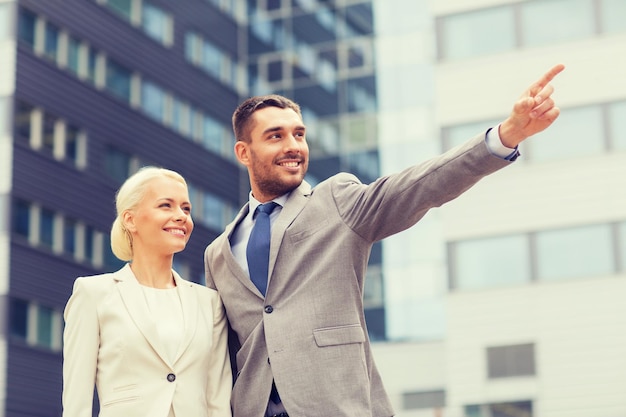 affari, partnership, successo gesto e concetto di persone - uomo d'affari sorridente e imprenditrice che punta il dito sopra l'edificio per uffici