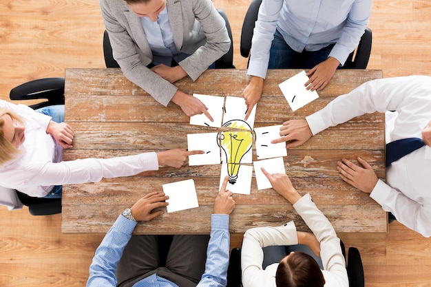 affari, persone in ufficio, avvio e concetto di lavoro di squadra - primo piano del team creativo seduto al tavolo e mettendo insieme pezzi di puzzle con foto di lampadina