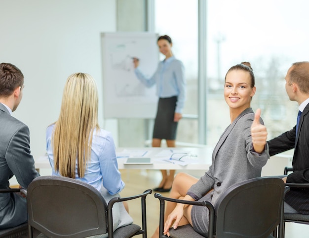 affari, ufficio e concetto di successo - donna d'affari sorridente con il team in ufficio che mostra i pollici in su