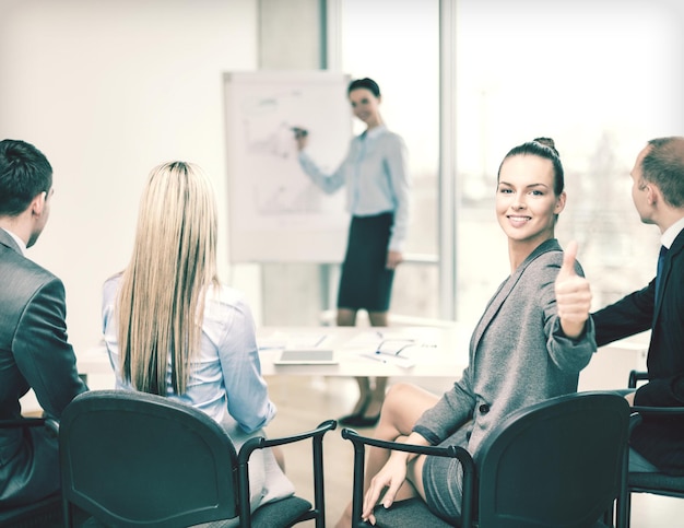 affari, ufficio e concetto di successo - donna d'affari sorridente con il team in ufficio che mostra i pollici in su