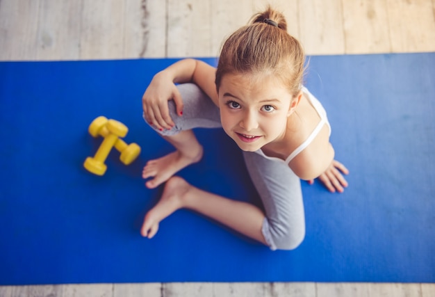 affascinante bambina è seduta sul tappetino yoga