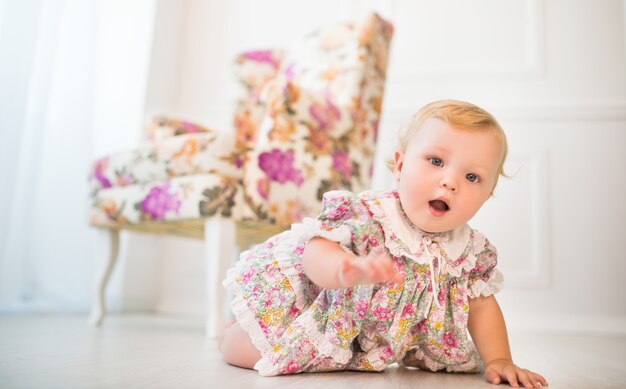 Affascinante bambina in abito floreale striscia sul pavimento di un bellissimo soggiorno elegante