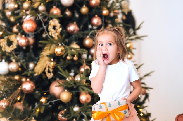 Affascinante bambina sorpresa tiene un regalo su uno sfondo di alberi di natale