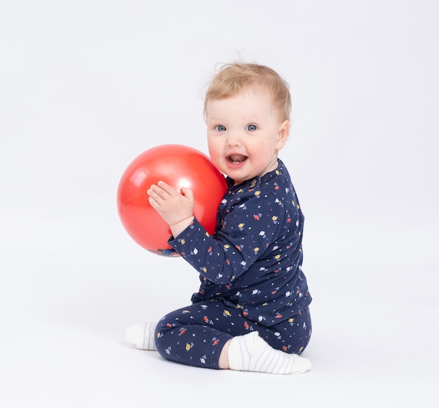 Affascinante bambino sorridente tiene una palla rossa su sfondo bianco