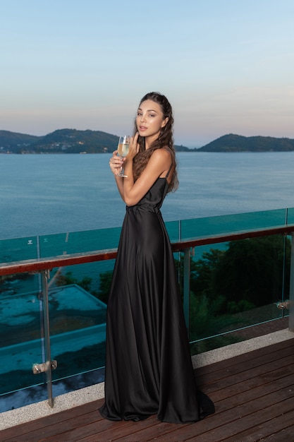 Affascinante bella ragazza in posa in un abito da sera al cioccolato con un bicchiere di champagne in mano