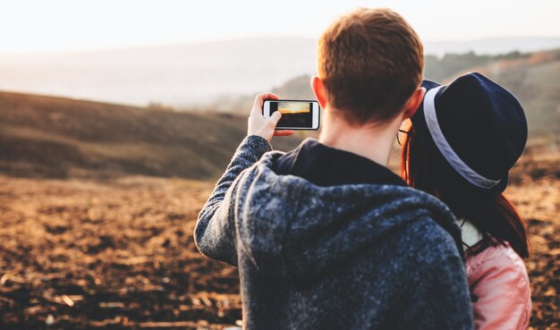 Affascinante coppia caucasica facendo un selfie mentre posa in un campo con occhiali e cappello