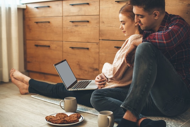 Affascinante coppia caucasica fare colazione in cucina sul pavimento mentre si guarda qualcosa al computer