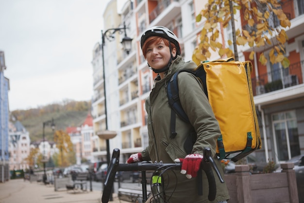 Affascinante corriere femminile che indossa il casco in bicicletta mentre si lavora in città sulla sua bicicletta